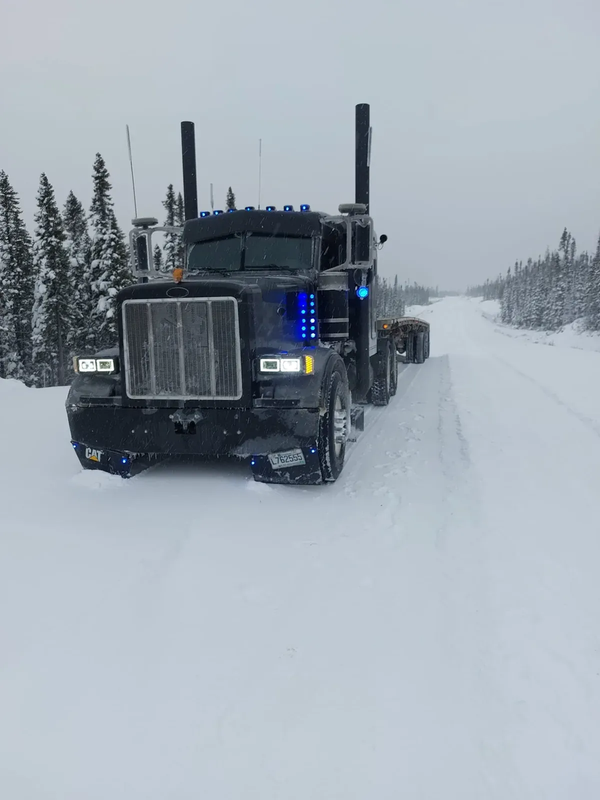 Peterbilt noir arrêté sur une route enneigée bordée d’épinettes