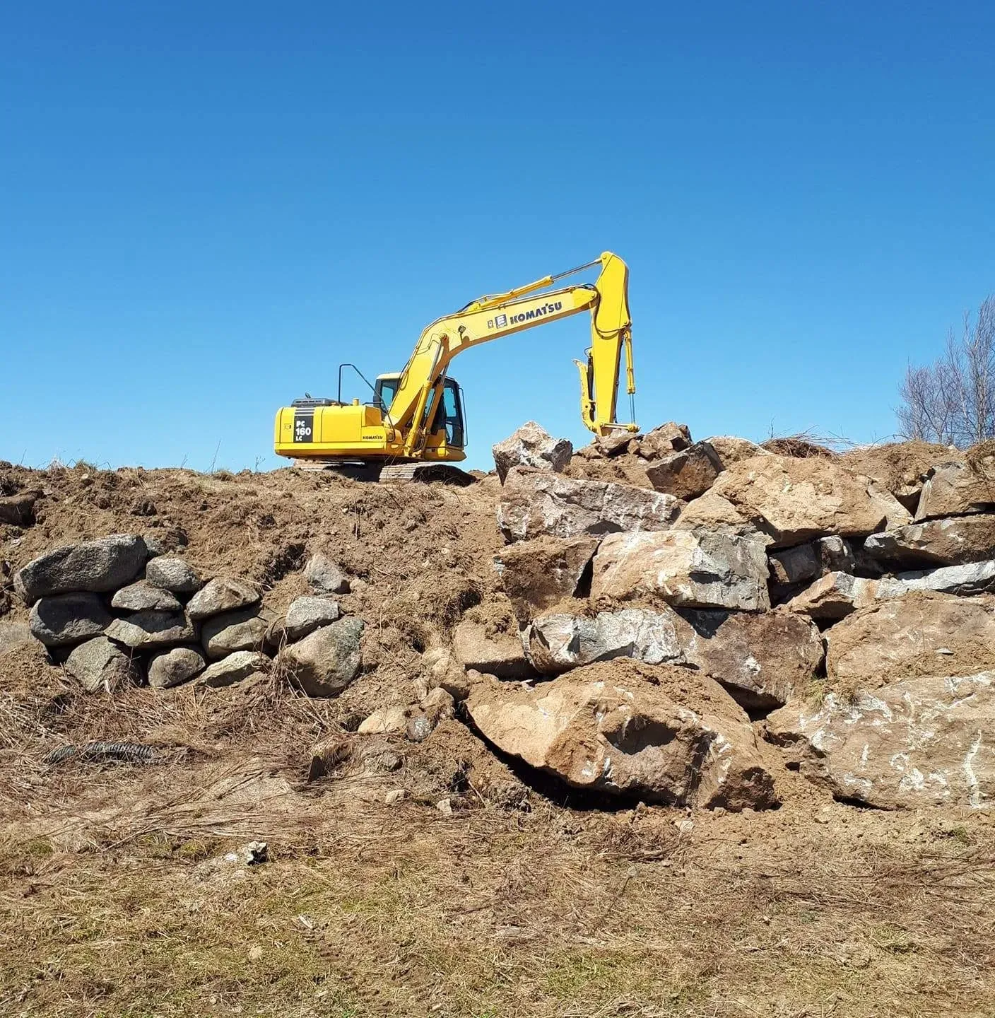 Pelle Komatsu PC160LC au sommet d’un tas de roche et de terre, sous un ciel bleu