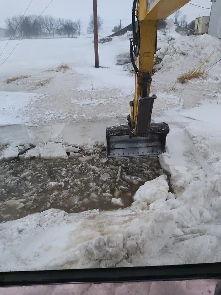 Godet de la pelle qui casse la glace dans une cour enneigée, vue depuis la cabine