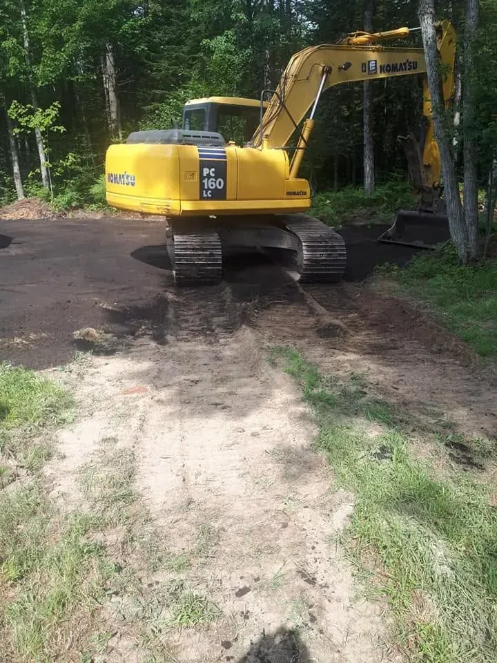 Pelle Komatsu PC160LC sur un terrain de terre noire fraîchement nivelé, en bordure de bois