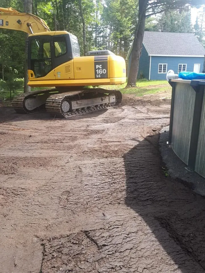 Pelle Komatsu PC160LC qui nivelle une cour à côté d’une maison et d’une piscine hors terre
